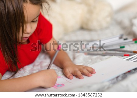 cute little child girl in red pajamas draws with pencils at home