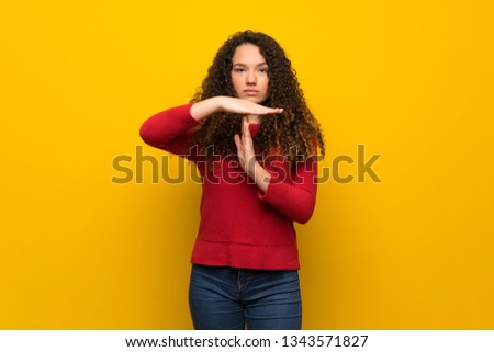Teenager girl with red sweater over yellow wall making time out gesture