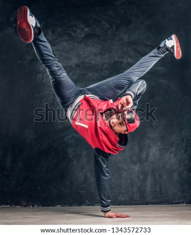 Emotional stylish dressed man performing break dance moves on the floor. Studio photo against a dark textured wall