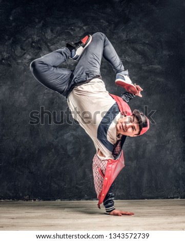 Hip-hop style dancer performs breakdance acrobatic elements. Studio photo against a dark textured wall