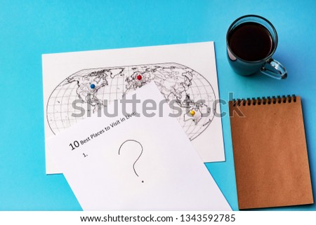 The inscription on a white sheet of A4: 10 best plases to visit in live. On a blue background with a cup of coffee, a notepad and a map of the world