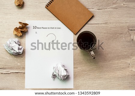 The inscription on a white sheet of A4: 10 best plases to visit in live. On a wooden background, ?up of coffee and notepad