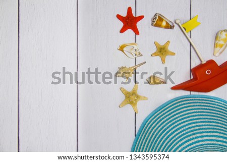 Concept of travel - toy boat, hat, various exotic shells and other sea treasures on a light wooden background with sand view from the top.