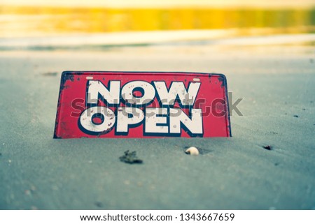 A business sign that says ‘Open’ on sand at beautiful beach background.