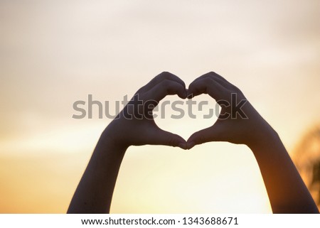Beautiful Silhouette hand made heart shape on the sunset background.
