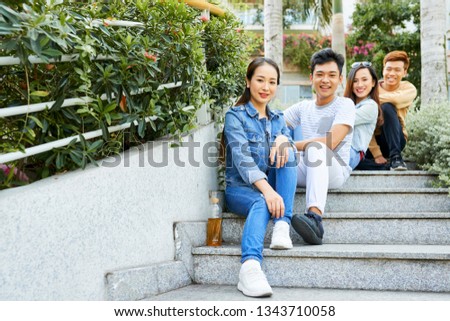 Group of happy young Asian people sitting on steps outdoors and looking at camera