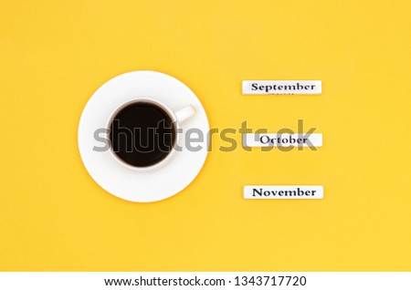 Wooden calendar autumn months September October November and Cup of black coffee aimed at September on yellow background. Concept Top view Flat Lay Copy space