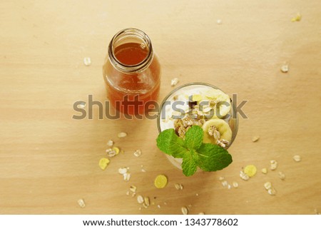 Glass of yoghurt with banana and Granola for healthy body  , Healthy home made food image with with honey  on wooden texture , selective focus
