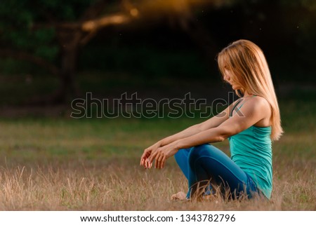 Relaxed woman sitting in lotus pose on grass in summer park