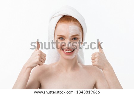 Beauty treatment. Woman applying moisturizing cream skin care product on face, making thumb up sign studio shot