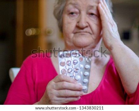 Elderly woman with beautiful wrinkled face is holding pills in her hands to choose medicines. Selective focus depth of field