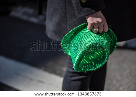 Woman in black coat holding green St. Patrick Day hat