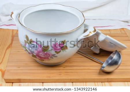 Empty vintage ceramic white painted tureen with open lid, stainless steel ladle on a wooden surface
