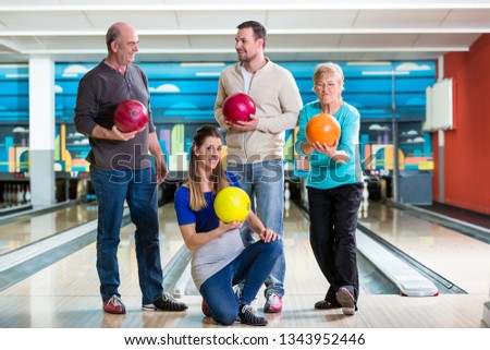 Smiling family holding multi colored bowling ball in club