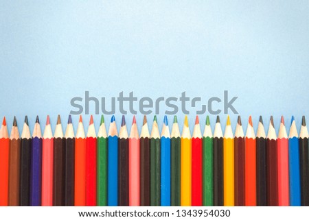 Color pencils laid out in a row on a blue background. Flat lay, top view
