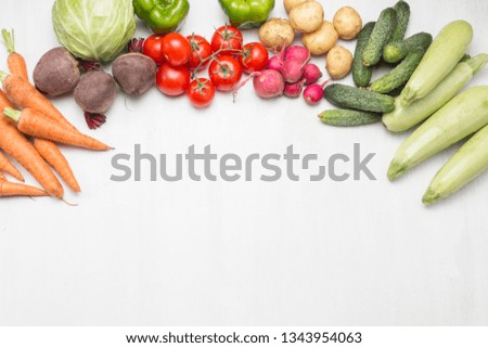 Little baby looks at fresh organic vegetables on a light wooden background. Care for health. Choice of the first food. Healthy baby food. Flat lay, top view