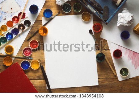 The Artist's Workplace with Watercolor Paint, Gouache, Brushes and Paper Sheets on a Wooden Background. The Creative Workshop concept. Copy space. Flat lay, top view