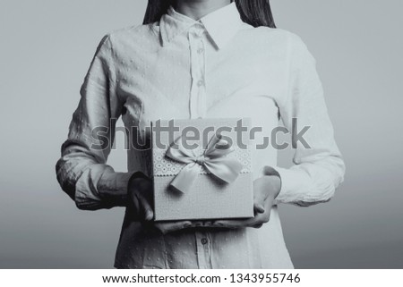 Young girl holding a gift in front of him. The face of the girl is not visible. Black and white image