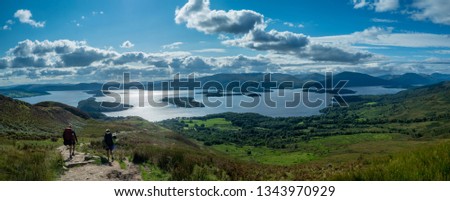 panorama of two girls hiking with beautiful lake (loch lomond) and green landscape on a sunny day Royalty-Free Stock Photo #1343970929
