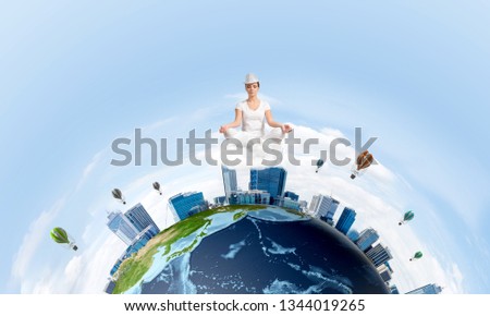 Young woman keeping eyes closed and looking concentrated while meditating on clouds in the air with panoramic view of Earth globe on background. Elements of this image are furnished by NASA