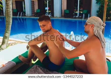 Man at pool rubs boyfriend's back with sunscreen