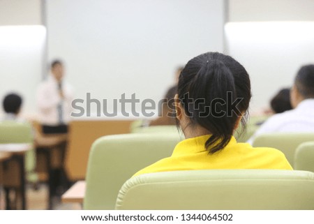 The lady with the yellow T-shirt is sitting on the chair and lecture in the classroom with blurred background.