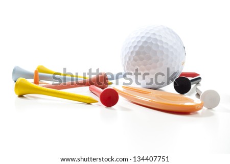 Miscellaneous parts used for playing golf: A ball, different colored tees, a pitch fork and a ball marker. Studio shot, shallow depth of field.