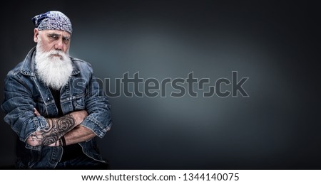 studio portrait of a senior hipster with tattooed arms, wearing a bandana and a long white beard. panoramic head Royalty-Free Stock Photo #1344140075