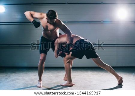 strong muscular shirtless mma fighter punching another while man doing clinch