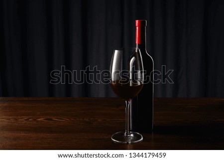 Wine bottle and glass with red wine on wooden surface
