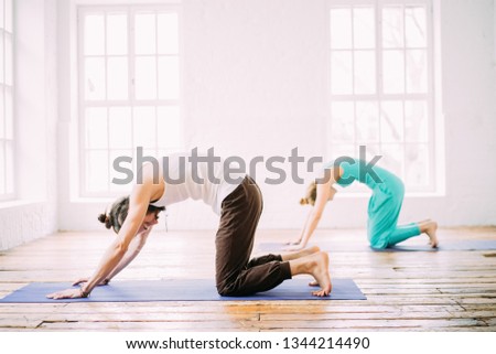 Sporty man and woman doing yoga in studio, with wooden floor and big windows. Freedom, health and yoga concept.