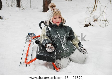 Boy sitting on snow with a sledge, winter cold day in the woods.