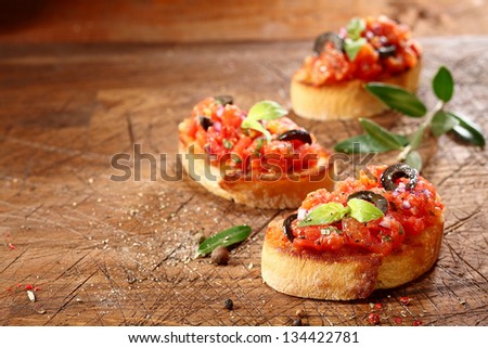 Preparing tasty Italian bruschetta with chopped vegetables and oil on grilled or toasted crusty baguette sprinkled with seasoning and spices on an old grungy scored wooden chopping board