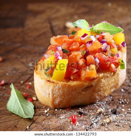 Cooking colourful bruschetta with toasted crispy sliced baguette topped with chopped tomato, onion, oil, seasoning and fresh basil on an old wooden table with scattered remnants of ingredients
