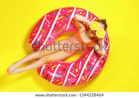 A little child girl in a swimwear suit lying on a donut inflatable circle. Yellow background. Top view. Summer concept.