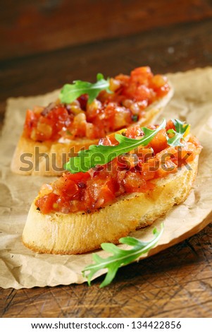 Tasty canape or bruschetta with chopped fresh tomato , onion and seasoning on crusty crisp toasted or grilled baguette garnished with a leaf of rocket on crumpled brown paper