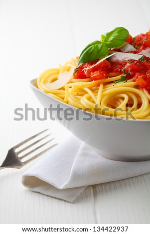 Close up shot of a white bowl of pasta with tomato sauce and fresh basil with a white napkin and fork.