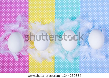 White eggs and feathers on colorful polka dots background. Happy Easter concept. Minimal style, flat lay.