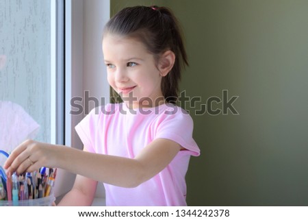 Beautiful caucasian white girl enthusiastically paints a picture with colored pencils. Smiling cute girl in pink T-shirt drawing a picture with pencils on blurred neutral background. Kid learning art
