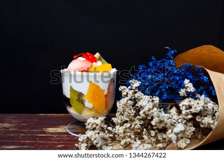 Fruit cakes are in a clear glass with blue dried flowers and white dried flowers on a black background.
