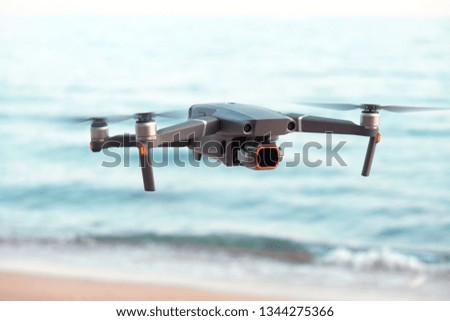 Professional filming drone flies in the air at a low altitude against a blue sky and sea sandy beach. Drone makes photos. Modern new technology. Ready background with place for your text.