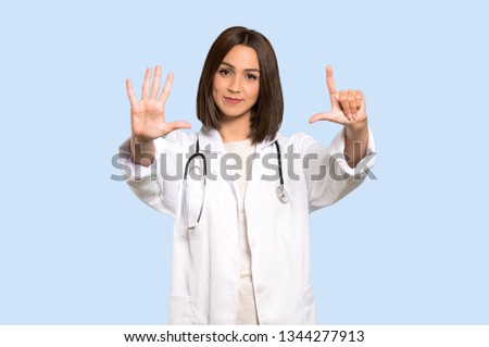 Young doctor woman counting seven with fingers on isolated blue background