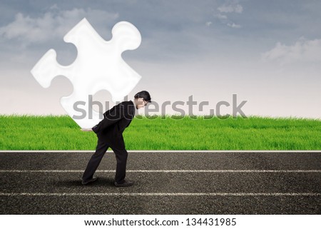 Asian businessman carry puzzle on the road under blue sky
