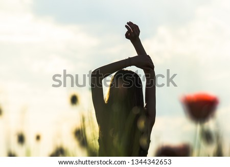 Silhouette of Girl rising hands against sun, flower field