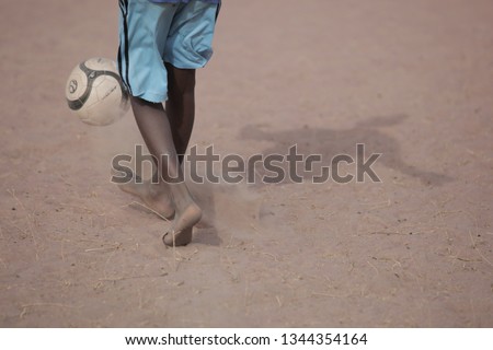 Jali, Gambia, Africa, May 18, 2017: wide angle photography of elementary school boy feet  playing football with new ball, barefoot on sandy field, outdoors on a sunny day 