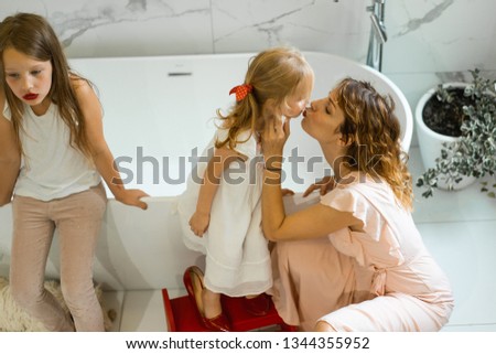 Mom and daughters do makeup in the bathroom, apply lipstick in front of the mirror. Daughters in her mother's heels. Mom and daughters have fun, spend time together.