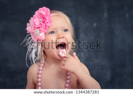 themed birthday for a fun emotional girl of the blonde 2 years old smash the cake in pink color on a black background. stylized photo session tradition with sweet decor and balloons