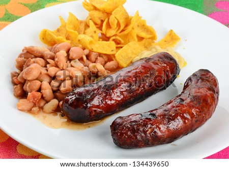 Grilled sausage and borracho beans on plate with corn chips against colorful Southwest design place mat-- typical cowboy food.