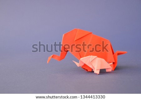 Two paper-folded elephants in pink and red stand on a blue background - concept with a little baby elephant and a mother elephant folded according to the origami technique