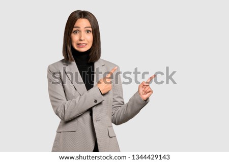 Young business woman frightened and pointing to the side on isolated grey background